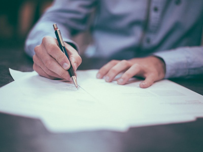 Hand with pen reviewing and annotating insurance policy paperwork on a desk