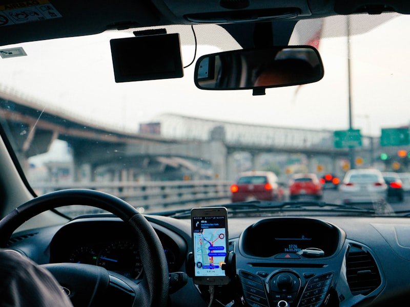 Driver's view inside vehicle with mounted smartphone showing GPS navigation route, dashcam overhead, highway ahead